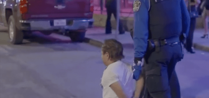 Police officer detaining person on street.